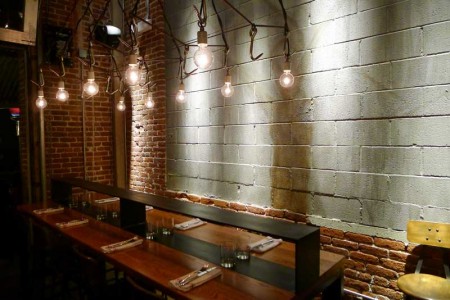 A communal table surrounded by exposed brick and hanging Edison lightbulbs at Bestia restaurant in downtown LA